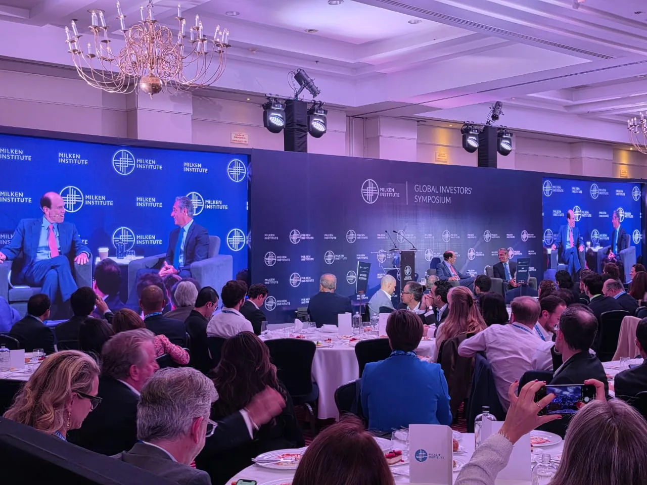Plenary session of the Milken Institute Global Investors Symposium at the Four Seasons Hotel Mexico City, with LED screens and stage lighting.